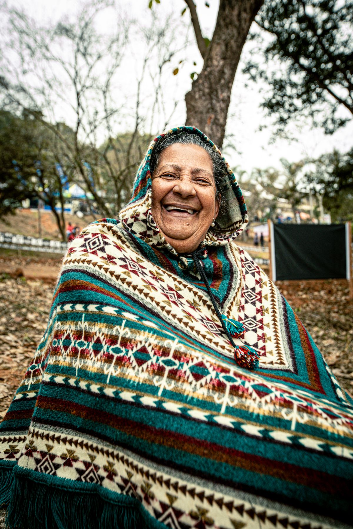 Senhora idosa rindo, agasalhada com um poncho colorido, ao ar livre