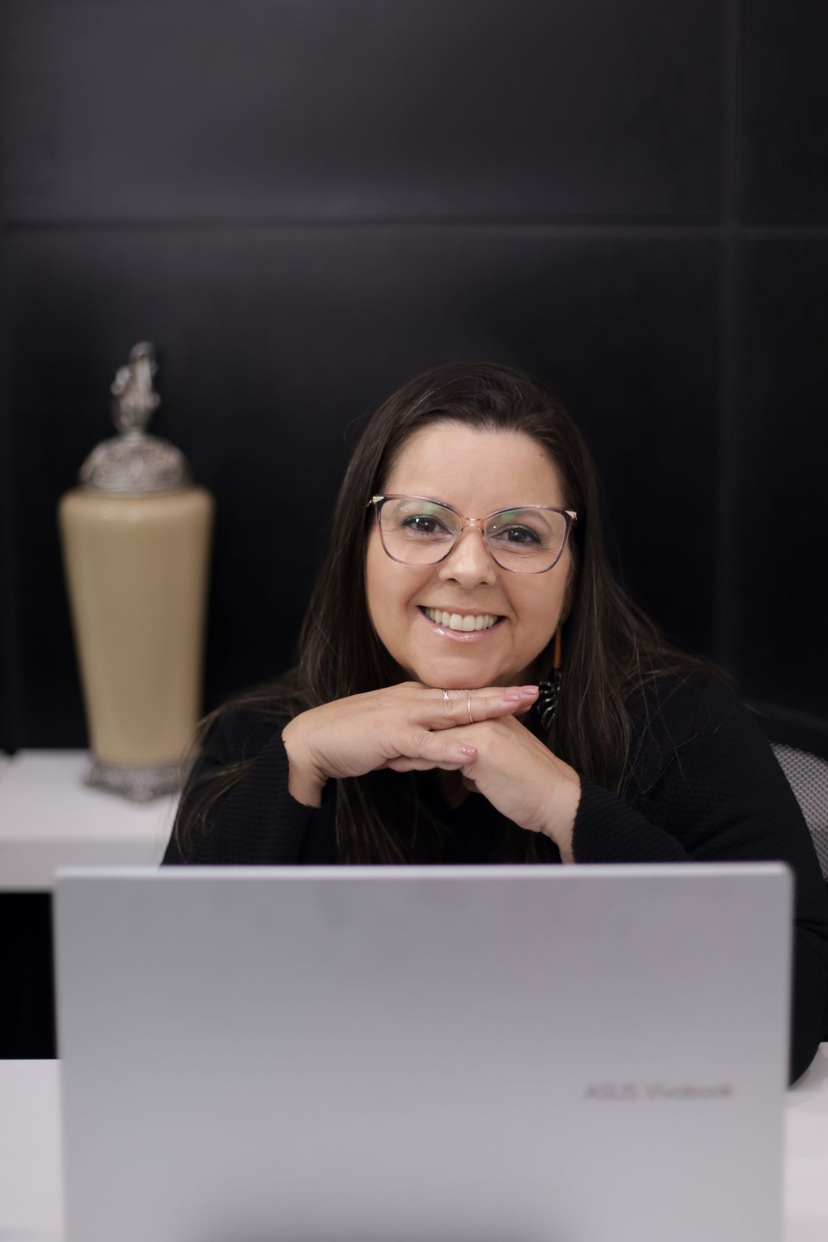 Consultora sorrindo durante um atendimento, apoiada na mesa atrás do notebook